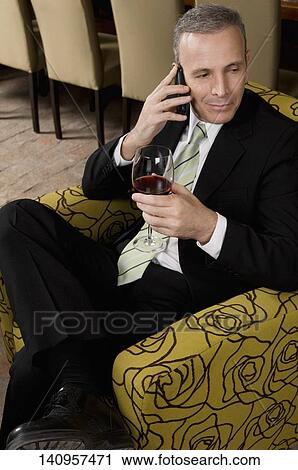 Businessman talking on a mobile phone and holding a wine glass View Large Photo Image Stock Image - Businessman talking on a mobile phone and holding a wine glass. Fotosearch