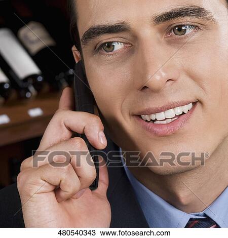 Stock Image - Businessman talking on a mobile phone in a bar. Fotosearch