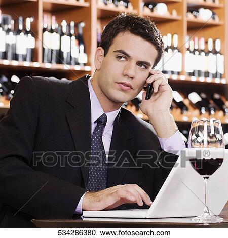 Stock Image - Businessman talking on a mobile phone and working on a laptop. Fotosearch