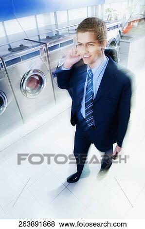 Stock Photo - Businessman talking on a mobile phone in a laundromat. Fotosearch