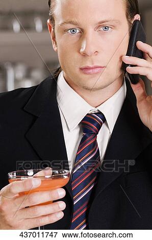 Businessman talking on a mobile phone and holding a cocktail glass View Large Photo Image Stock Photo - Businessman talking on a mobile phone and holding a cocktail glass. Fotosearch