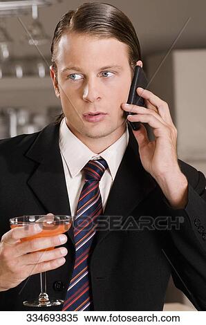 Businessman talking on a mobile phone and holding a cocktail glass View Large Photo Image Stock Photography - Businessman talking on a mobile phone and holding a cocktail glass. Fotosearch