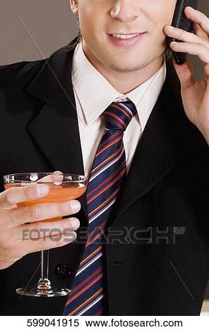 Businessman talking on a mobile phone and holding a glass of cocktail View Large Photo Image Stock Photography - Businessman talking on a mobile phone and holding a glass of cocktail. Fotosearch