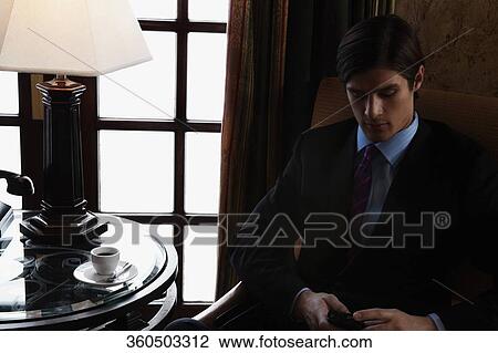 Stock Image - Businessman text messaging on a mobile phone, Biltmore Hotel, Coral Gables, Florida, USA. Fotosearch