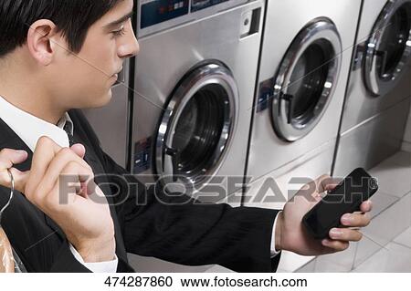 Stock Image - Businessman text messaging on a mobile phone in a laundromat. Fotosearch