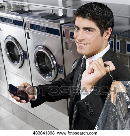 Stock Photo - Businessman text messaging on a mobile phone in a laundromat. Fotosearch