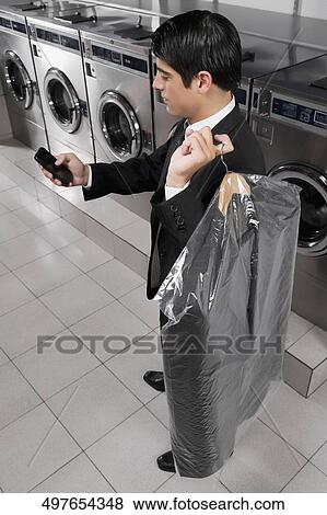 Businessman text messaging on a mobile phone in a laundromat View Large Photo Image Stock Photo - Businessman text messaging on a mobile phone in a laundromat. Fotosearch