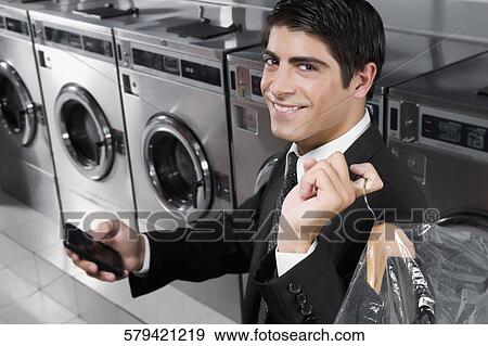 Stock Photo - Businessman text messaging on a mobile phone in a laundromat. Fotosearch