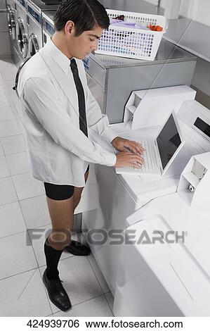 Businessman working on a laptop in a laundromat View Large Photo Image Stock Photograph - Businessman working on a laptop in a laundromat. Fotosearch