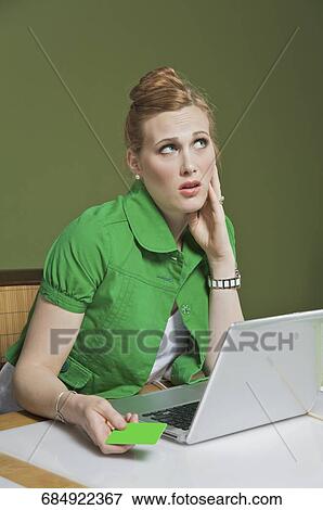 Stock Photo - Businesswoman holding a credit card and thinking in the office. Fotosearch