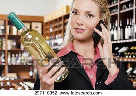 Stock Image - Businesswoman talking on a mobile phone and holding a wine bottle. Fotosearch
