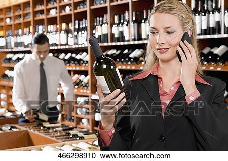 Businesswoman talking on a mobile phone and holding a wine bottle View Large Photo Image Stock Image - Businesswoman talking on a mobile phone and holding a wine bottle. Fotosearch
