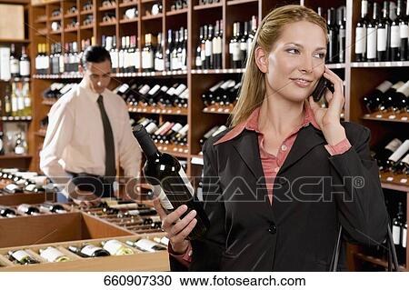 Stock Image - Businesswoman talking on a mobile phone and holding a wine bottle. Fotosearch