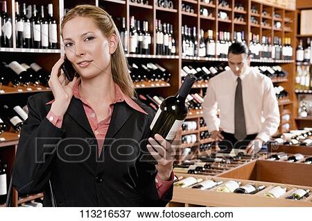 Stock Photo - Businesswoman talking on a mobile phone and holding a wine bottle. Fotosearch