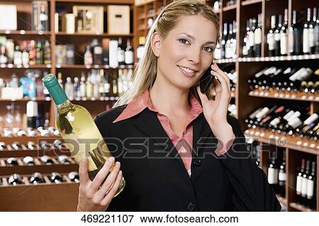 Businesswoman talking on a mobile phone and holding a wine bottle View Large Photo Image Stock Photo - Businesswoman talking on a mobile phone and holding a wine bottle. Fotosearch