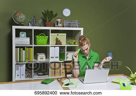 Stock Image - Businesswoman working on a laptop in the office and holding credit cards. Fotosearch