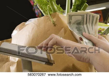 Stock Photo - Cashier holding money at a checkout counter in a supermarket. Fotosearch