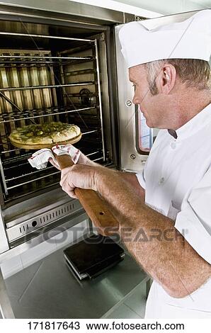 Stock Image - Chef putting a pizza into an oven. Fotosearch