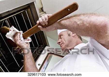 Stock Image - Chef putting a pizza into an oven. Fotosearch