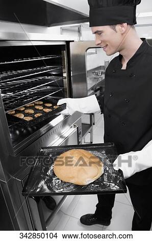 Picture - Chef taking out a bun and cookies from an oven. Fotosearch