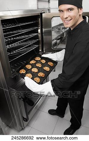 Chef taking out a tray of cookies from an oven View Large Photo Image Stock Image - Chef taking out a tray of cookies from an oven. Fotosearch