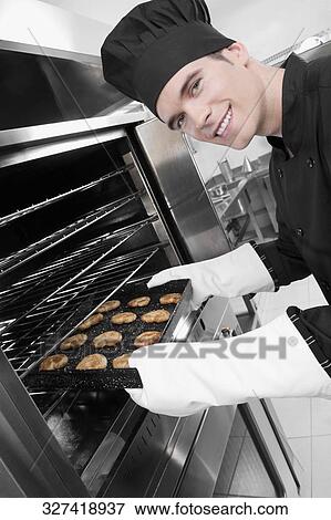 Stock Photo - Chef taking out a tray of cookies from an oven. Fotosearch