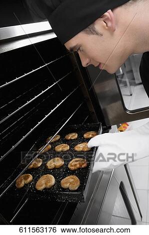 Chef taking out a tray of cookies from an oven View Large Photo Image Stock Photograph - Chef taking out a tray of cookies from an oven. Fotosearch