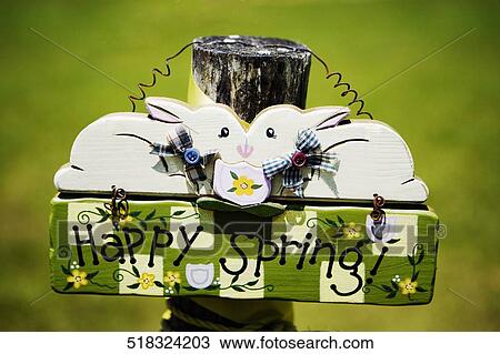 Stock Image - Close-up of a Happy Spring greeting sign hanging on a wooden post. Fotosearch