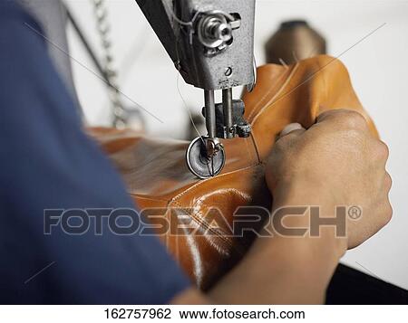 Stock Image - Close-up of a person's hand using a sewing machine in a shoe factory. Fotosearch
