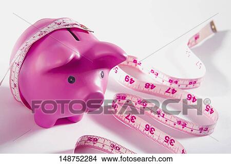 Picture - Close-up of a piggy bank wrapped with a tape measure. Fotosearch
