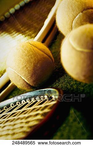 Stock Photography - Close-up of three tennis balls with two tennis rackets in a court. Fotosearch
