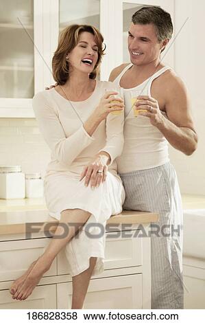 Couple drinking juice and romancing in the kitchen View Large Photo Image Stock Photo - Couple drinking juice and romancing in the kitchen. Fotosearch