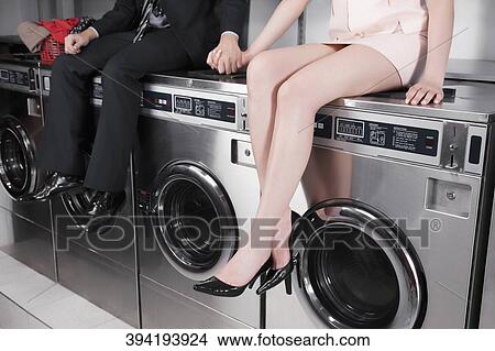 Picture - Couple holding hands and sitting on washing machines. Fotosearch