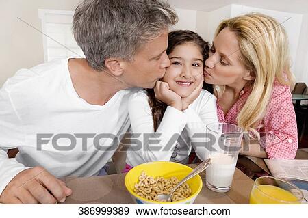 Stock Photo - Couple kissing their daughter at a breakfast table. Fotosearch