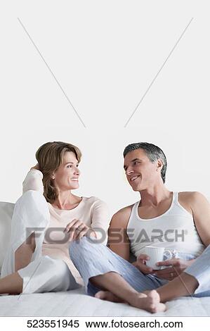 Stock Photography - Couple reclining on the bed and talking to each other. Fotosearch