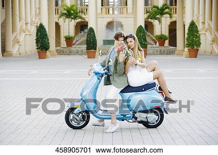 Stock Image - Couple sitting on a moped, Biltmore Hotel, Coral Gables, Florida, USA. Fotosearch