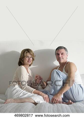 Stock Photo - Couple sitting on the bed and smiling. Fotosearch