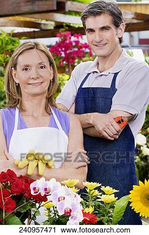Stock Image - Couple standing with their arm crossed in a greenhouse. Fotosearch