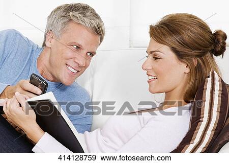 Stock Photo - Couple text messaging and reading a book. Fotosearch
