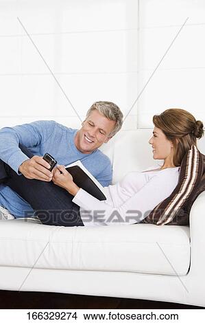 Couple text messaging and reading a book on the couch View Large Photo Image Picture - Couple text messaging and reading a book on the couch. Fotosearch