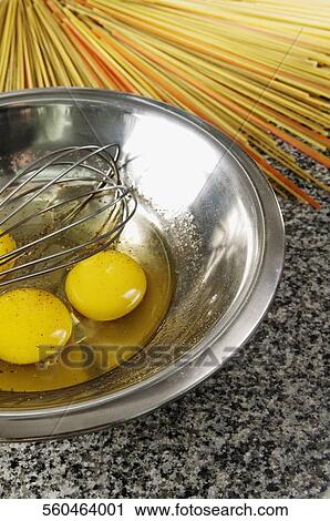 Stock Image - Egg yolk and an egg beater in a bowl with spaghetti. Fotosearch