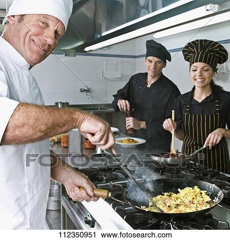 Stock Image - Female and a male chef cooking food in the kitchen. Fotosearch