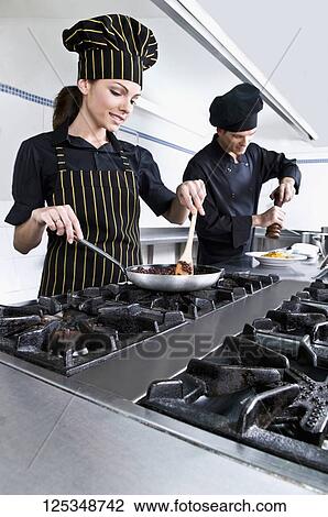 Stock Image - Female and a male chef cooking food in the kitchen. Fotosearch