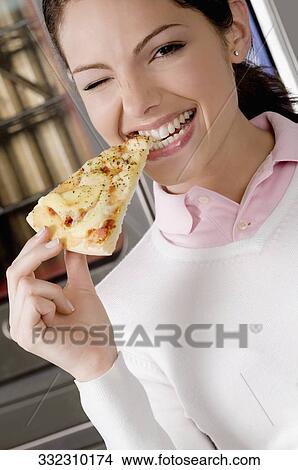 Picture - Female chef eating a slice of pizza. Fotosearch