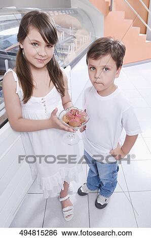 Girl holding a glass of ice cream and standing with her brother View Large Photo Image Stock Photograph - Girl holding a glass of ice cream and standing with her brother. Fotosearch