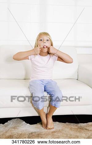 Stock Photograph - Girl sitting on a couch and making a funny face. Fotosearch