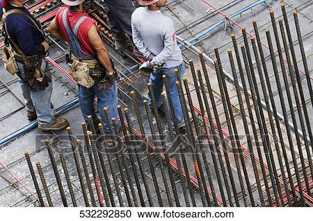 Stock Image - High angle view of four construction workers standing at a construction site. Fotosearch