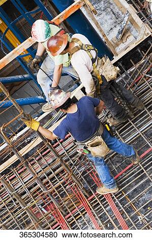 Stock Image - High angle view of three construction workers working at a construction site. Fotosearch