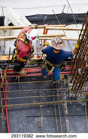 Stock Image - High angle view of two construction workers standing at a construction site. Fotosearch