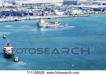 High angle view of two container ships with tugboats in the sea in front of a commercial dock View Large Photo Image Stock Photo - High angle view of two container ships with tugboats in the sea in front of a commercial dock. Fotosearch